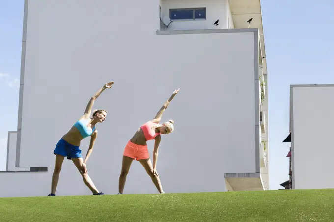 Two young female athletes stretching in park