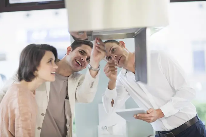 Mid adult couple and salesman looking at extractor hood in kitchen showroom