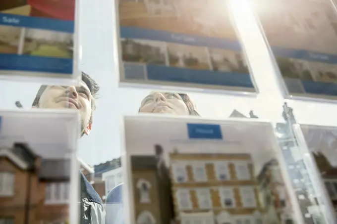 Couple contemplatively browsing real estate listings in a shop window.