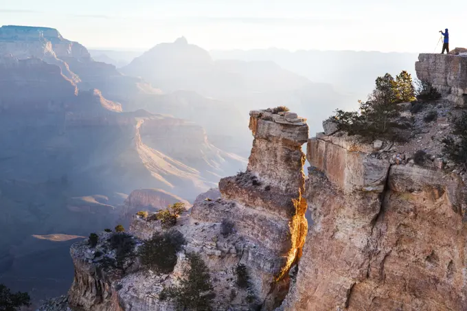 An adventurer stands atop a cliff enjoying the vast beauty of the Grand Canyon at sunrise.