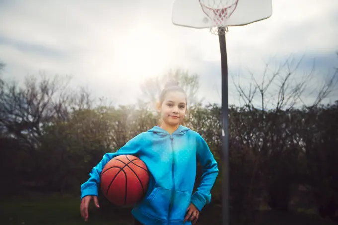 Young girl poised to play basketball under a sunny sky