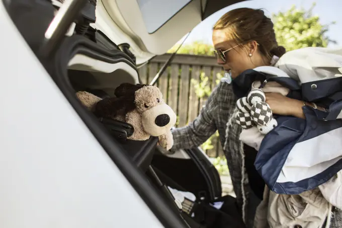 Busy mom packing the car with a stuffed toy and baby essentials.