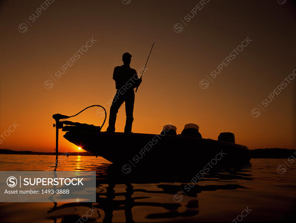 Silhouette of a man fishing at dusk - SuperStock