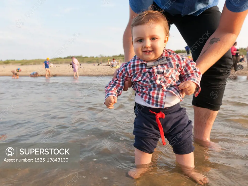 Young father holding his child over sea water having fun together. Son and parent bond