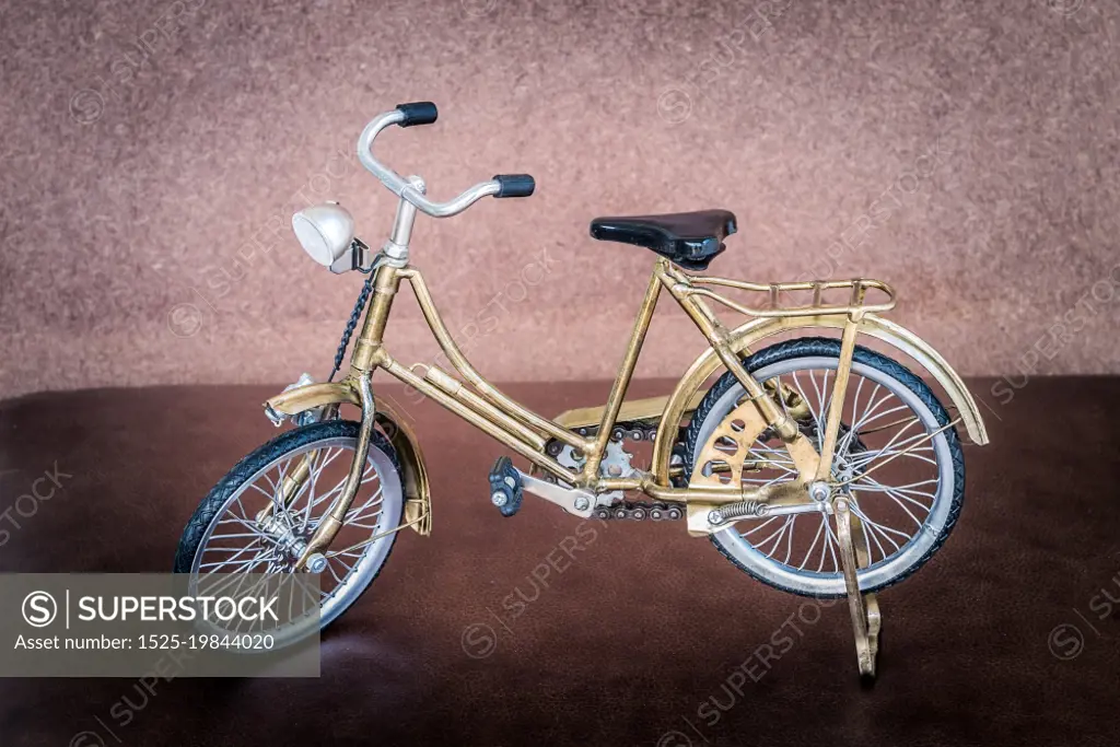 Small gold color toy bicycle on brown leather cushion