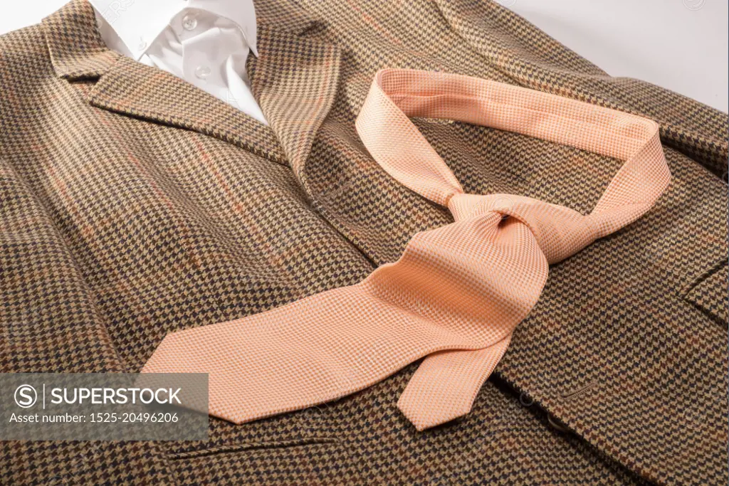 An orange and white dotted tie , already in a knot, lies on a brown sports jacket together with a white color shirt.