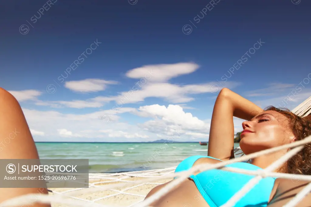 Woman in hummock on tropical beach. Young beautiful woman resting in hummock on tropical beach