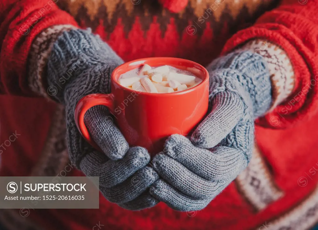 Warm winter photo which hands in knitted gloves holding a mug cocoa with marshmallow. Cocoa with marshmallow