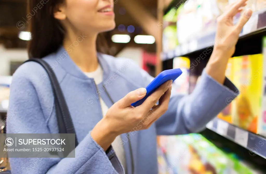 sale, shopping, consumerism and people concept - happy young woman with smartphone choosing and buying food in market