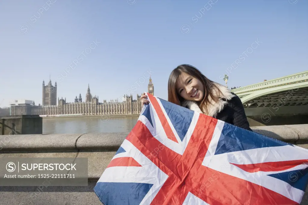 Portrait of happy woman holding British flag against Big Ben at London; England; UK