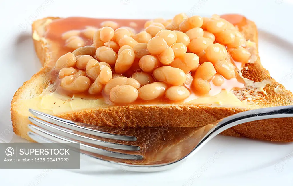 Extreme close-up on a plate of beans on toast with a fork.