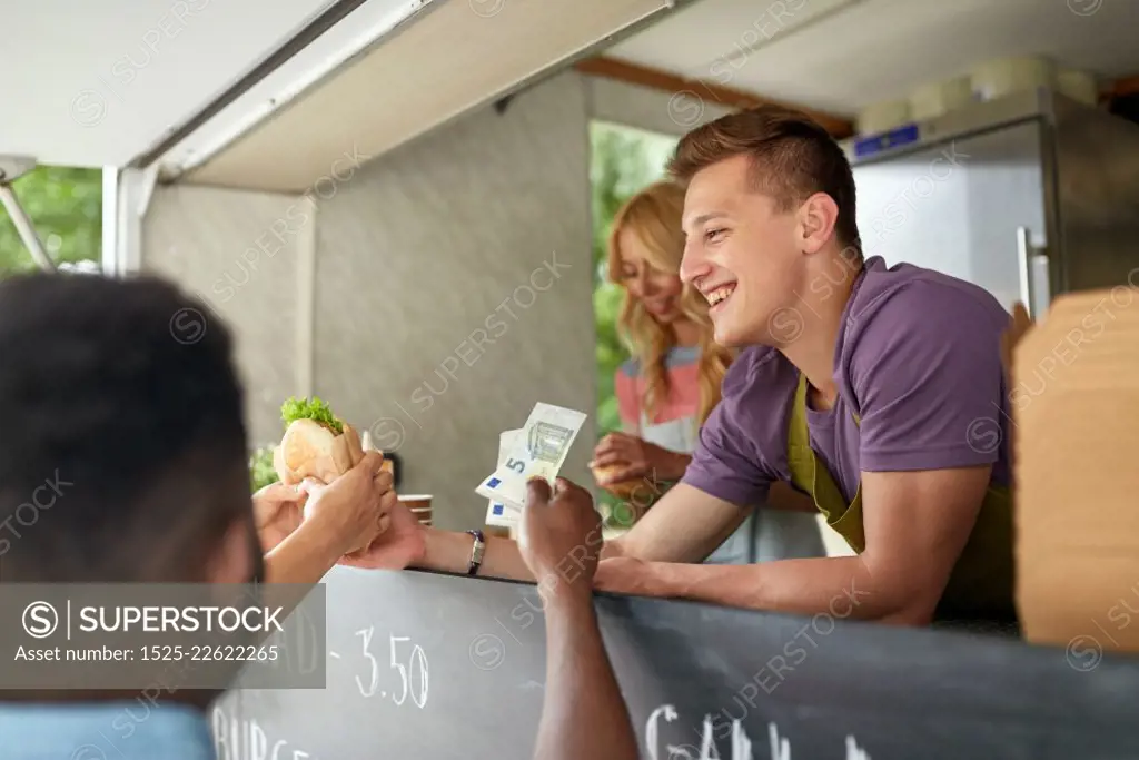 street sale, eating and people concept - happy salesman selling hamburgers at food truck and customers paying money. happy salesman selling hamburgers at food truck