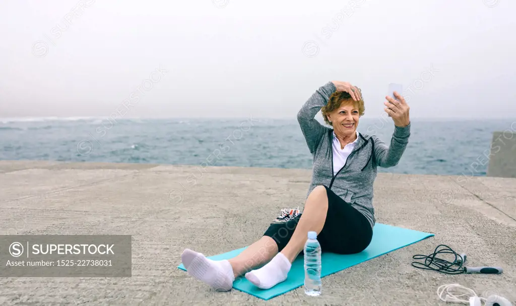 Senior sportswoman taking selfie by sea pier. Senior sportswoman taking selfie