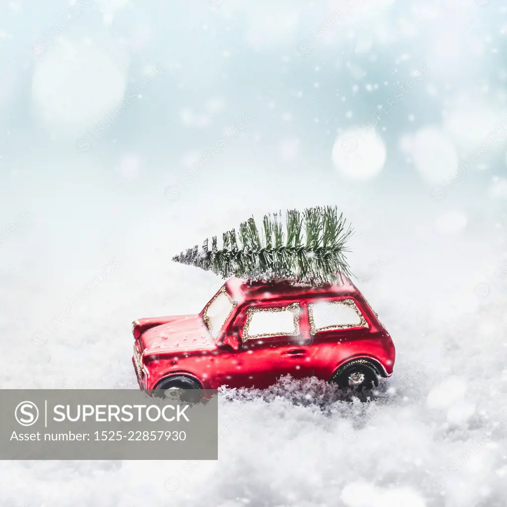 Christmas tree on red toy retro car in snow, through snowy winter wonder land with snowfall and bokeh. Creative Christmas holiday concept. Copy space for your greeting and design. 