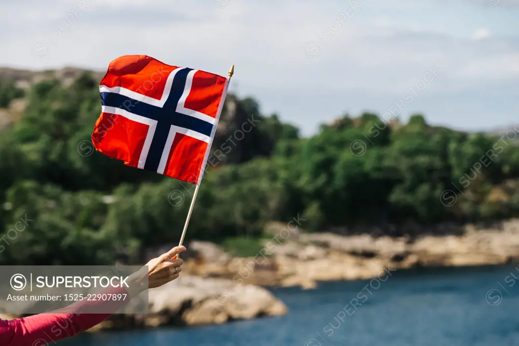 Tourist hand holding norwegian flag on rocky stone sea coast background.. Tourist with norwegian flag on sea coast