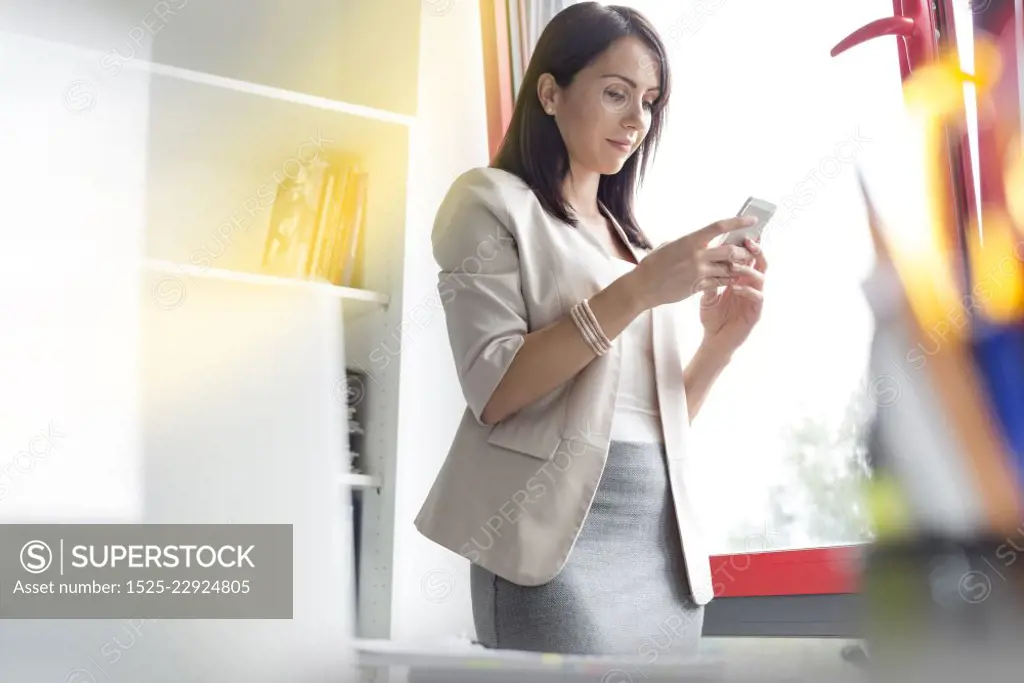 Businesswoman texting on smartphone by window at office