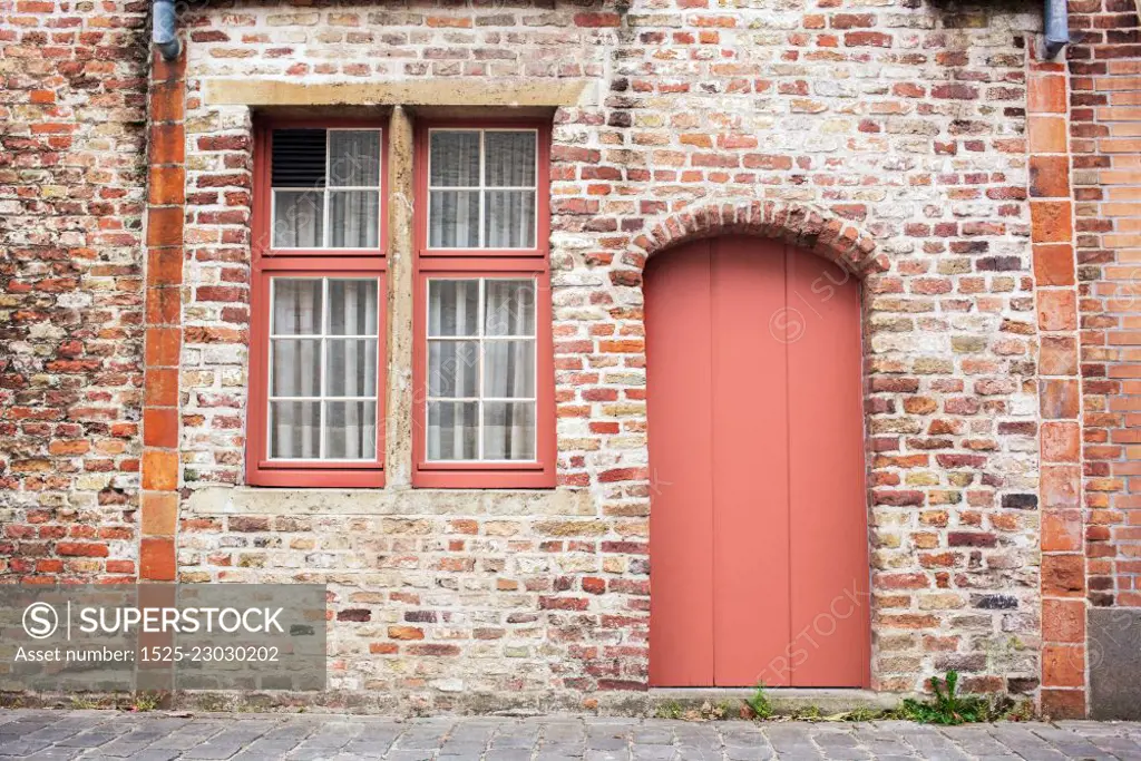 Freshly painted door on old European stone house of Bruges, Belgium in a color of the year 2019 Living Coral Pantone.. Facade brick old wall with painted door in a trendy color of the year 2019 Living Coral Pantone.