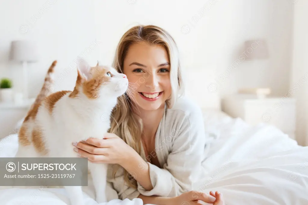 pets, morning, comfort, rest and people concept - happy young woman with cat in bed at home