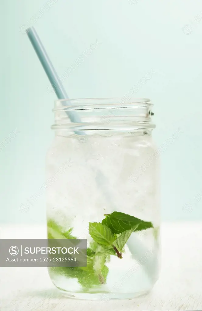 glass of cold water with fresh mint leaves and ice cubes on turquoise background