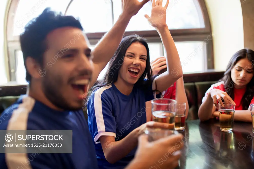 sport and entertainment concept - happy football fans or friends drinking beer, making high five and celebrating victory at bar or pub, supporting two teams with different shirt color