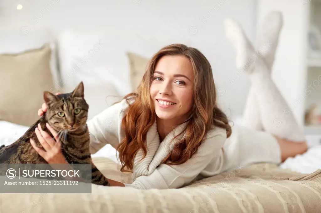 pets, comfort, rest and people concept - happy young woman with cat lying in bed at home