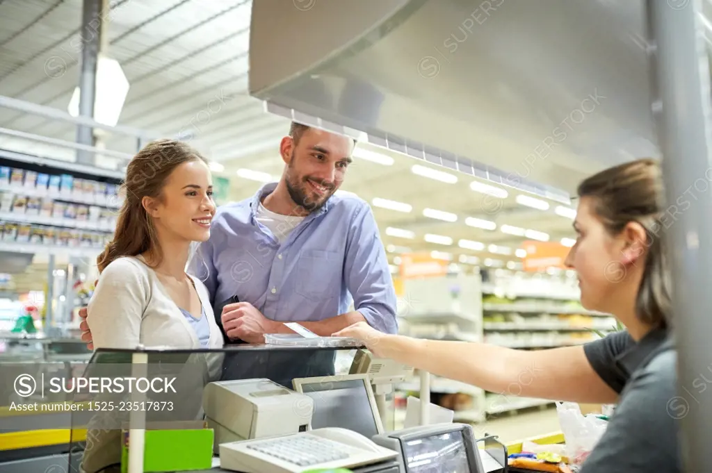 shopping, sale, consumerism, payment and people concept - happy couple buying food at grocery store or supermarket cash register and cashier taking money