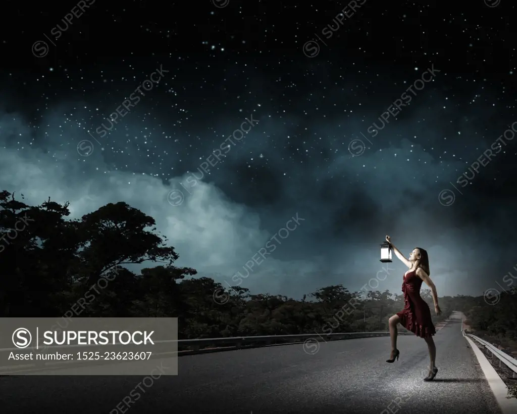 In search of something. Young attractive woman in red dress with lantern walking in darkness