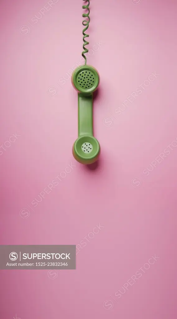 Green Vintage Retro Telephone Handset Hanfing on Pink background. Old Object from 1980-1990, Technology and Communication in the Past. Clean, Colourful  and Minimal