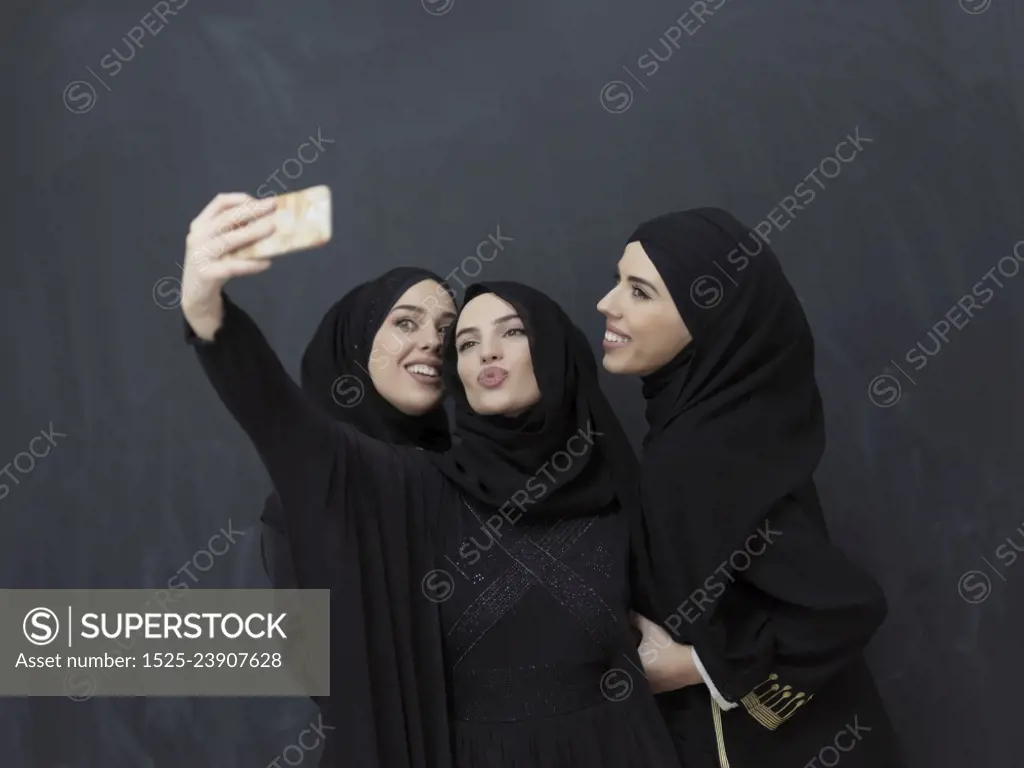 Portrait of Arab women wearing traditional clothes or abaya. Young muslim girls taking selfie in front of black chalkboard representing islamic arabic fashion and ramadan kareem concept