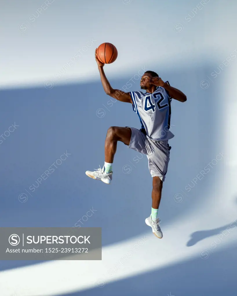 Basketball player with ball shows his skill in studio, high jump in action, neon background. Professional male baller in sportswear playing sport game, tall sportsman. Basketball player with ball, high jump in action