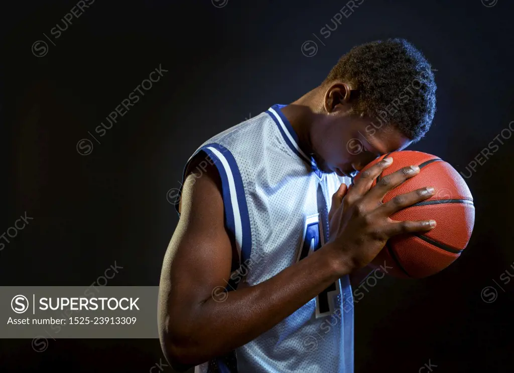 Focused basketball player poses with ball in studio, black background. Professional male baller in sportswear playing sport game, tall sportsman. Focused basketball player with ball in studio