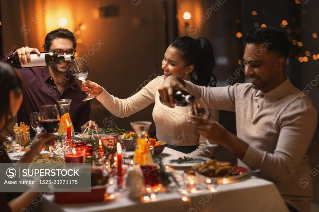 holidays, party and celebration concept - multiethnic group of happy friends having christmas dinner at home and drinking wine. happy friends drinking wine at christmas party