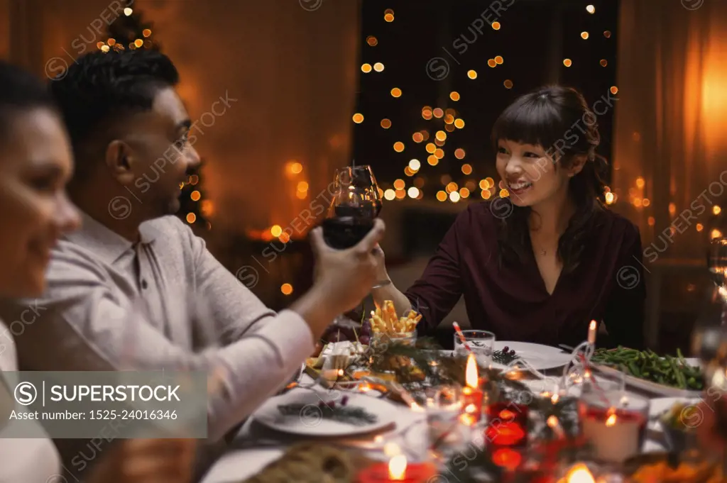 holidays, party and celebration concept - multiethnic group of happy friends having christmas dinner at home and drinking wine. happy friends drinking wine at christmas party