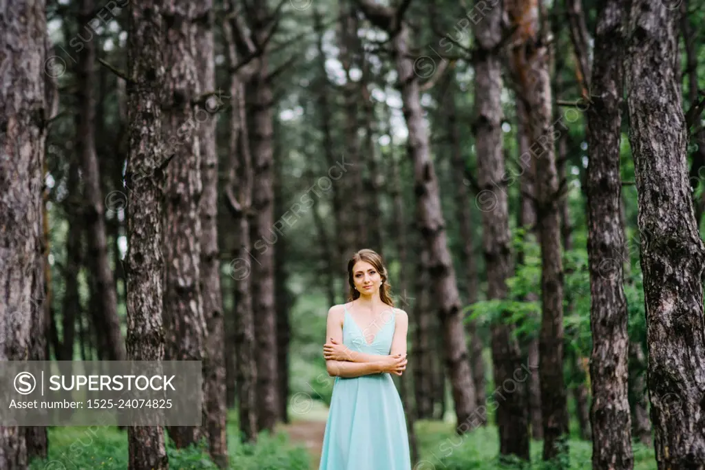 Happy girl in a turquoise long dress in a green park on a background of herbs, trees and rose bushes