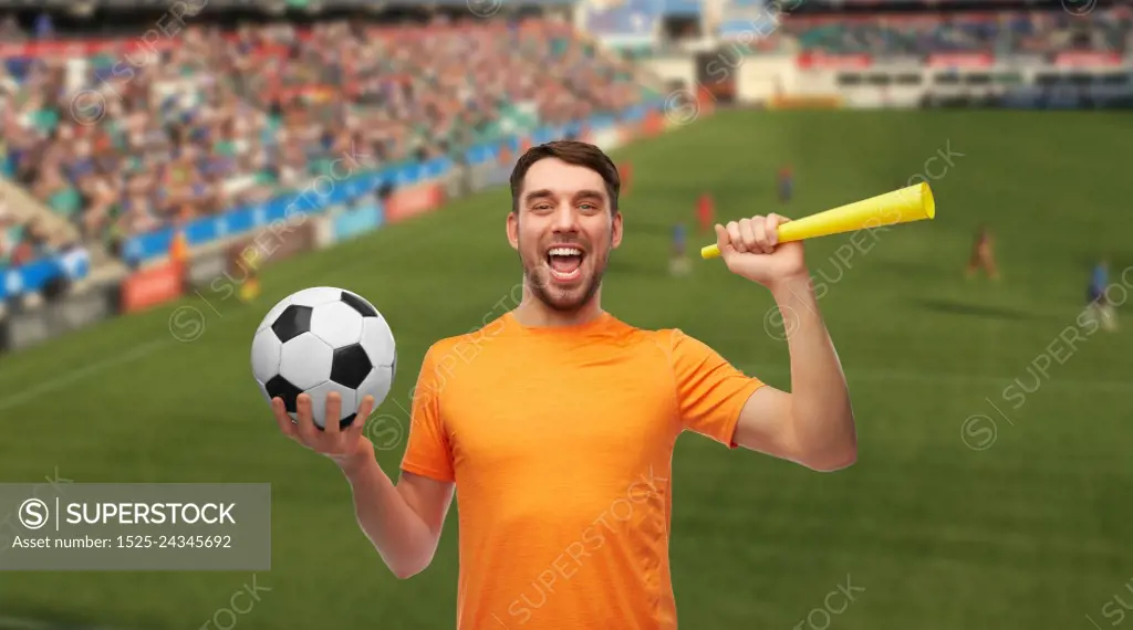 sport, leisure games and success concept - happy smiling man or football fan with soccer ball and vuvuzela over stadium background. male football fan with soccer ball and vuvuzela