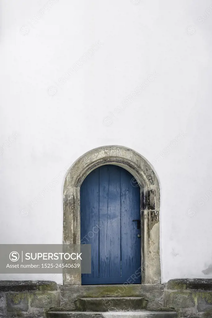 Medieval arched door. Aged wooden door in blue color with stone stairs and white wall. Just one door and an empty white house wall. Old blue entrance.