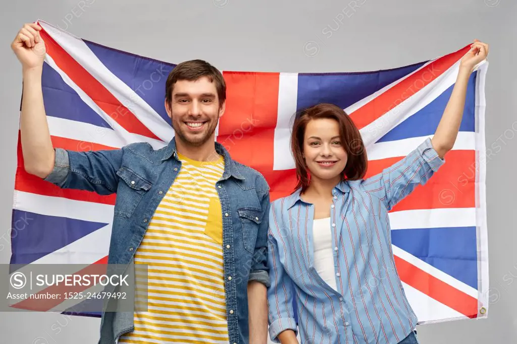 patriotism and national concept - happy couple holding british flag over grey background. happy couple holding british flag