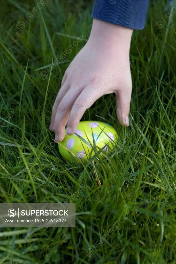 Child&acute;s hand about to pick up an Easter egg hidden in the grass