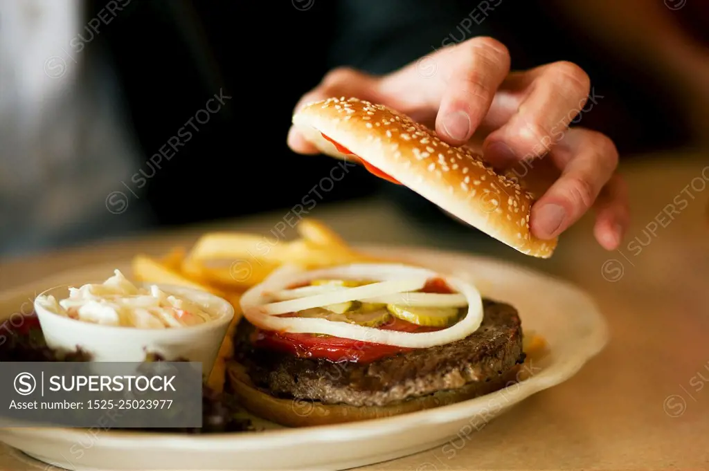 Man in a restaurant or diner eating a hamburger opening it to look inside, shot with available light, very selective focus