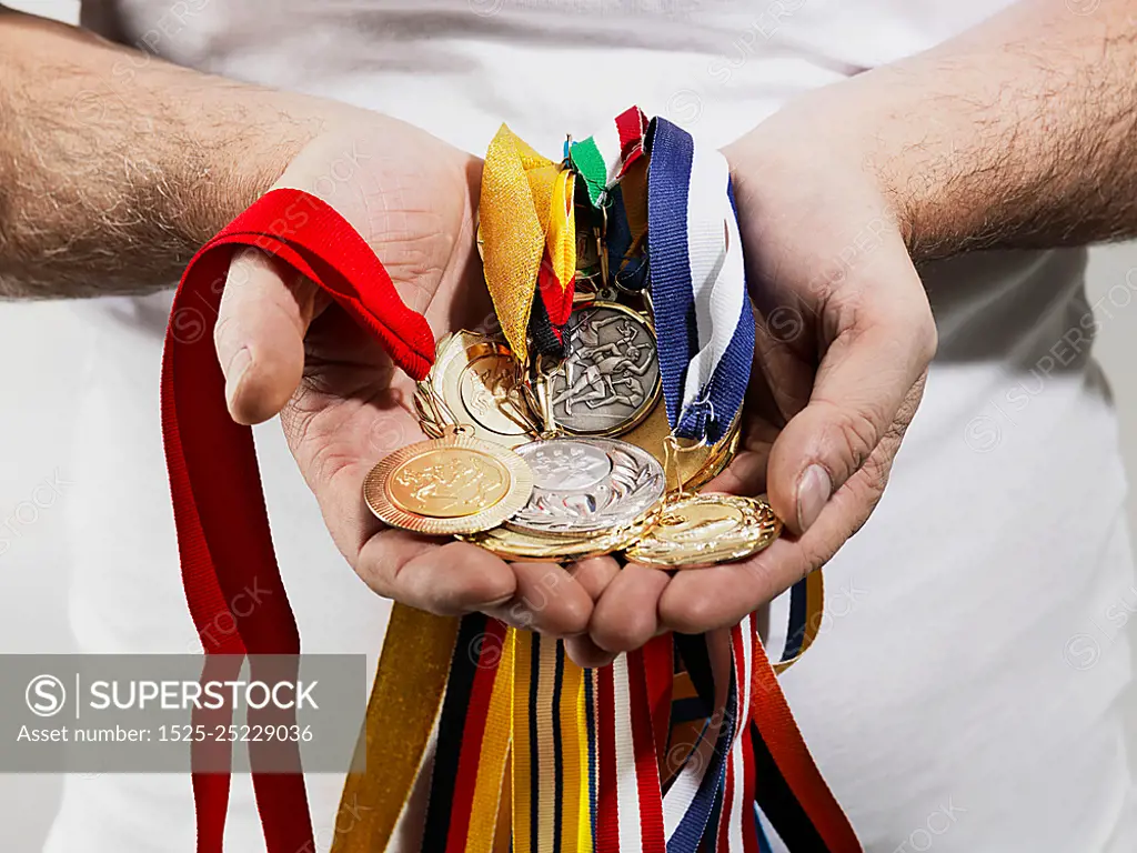 Mature man holding gold medals against white background