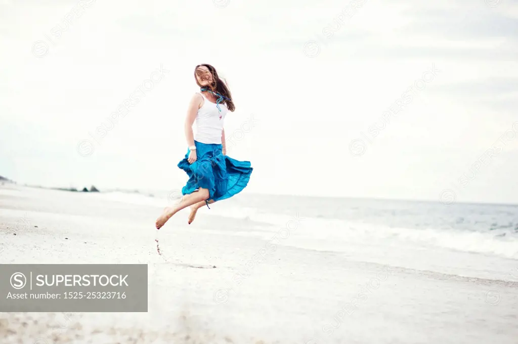 Young beautiful woman in white cami and turquoise skirt has fun on the ocean shore