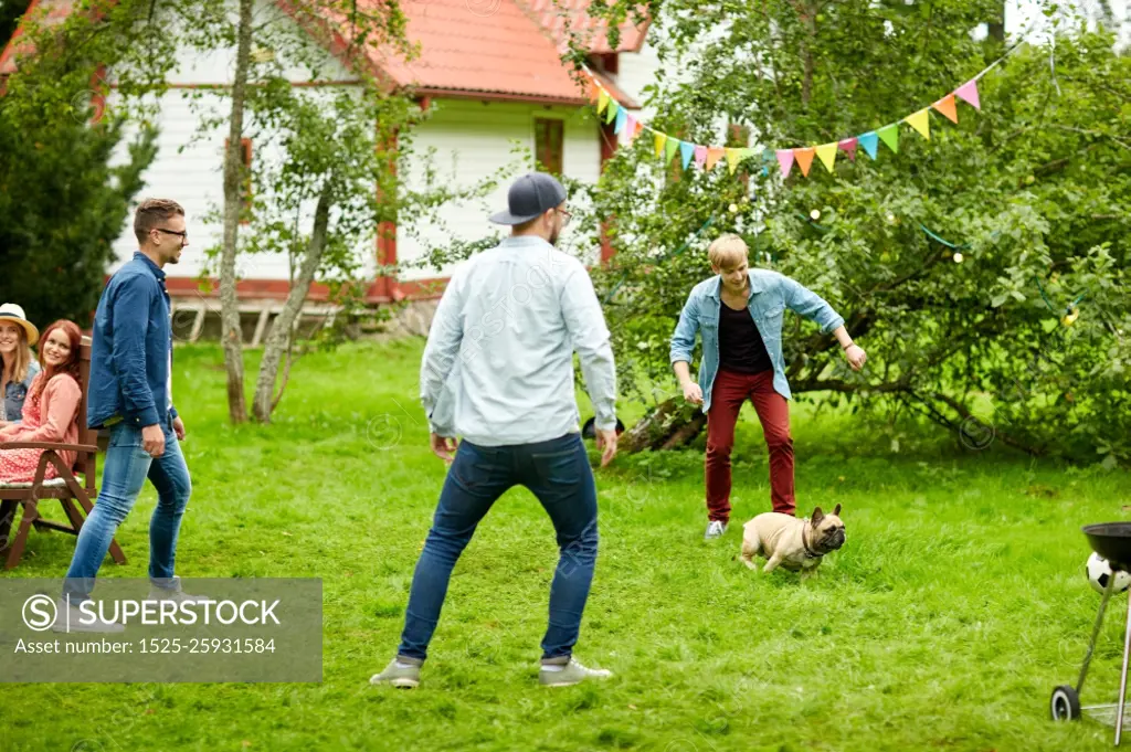 leisure, holidays, people and pets concept - happy friends playing with dog at summer garden party