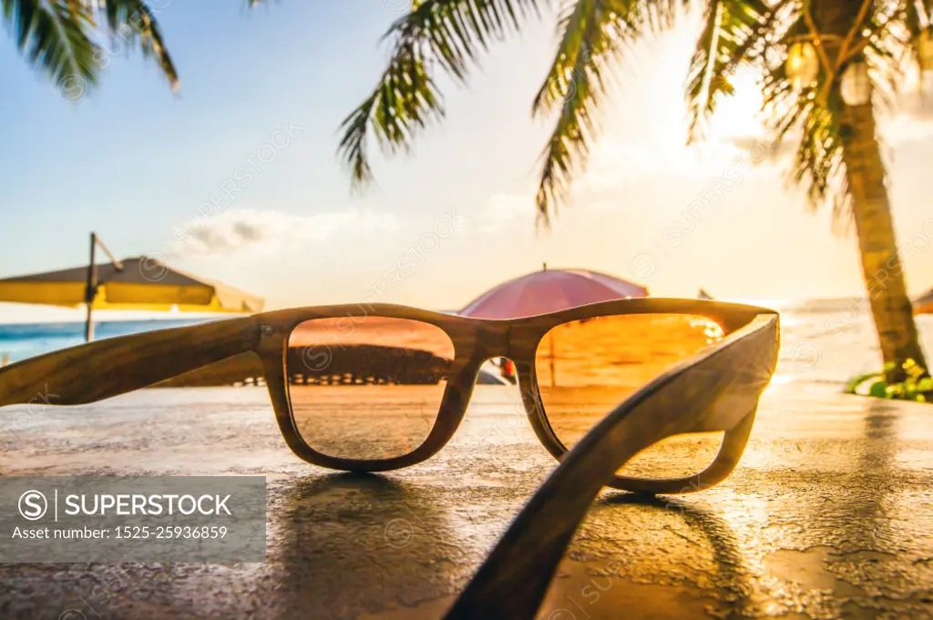 Sunglasses on beach. Sunglasses on tropical beach with palms at sunset