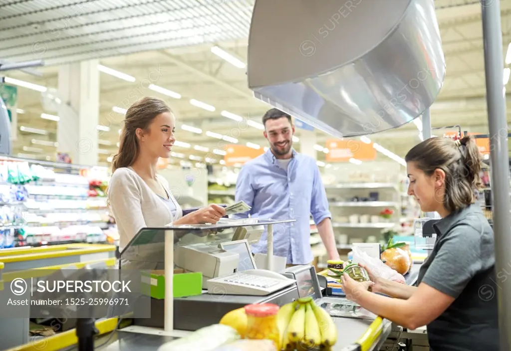 shopping, sale, consumerism and people concept - happy couple buying food at grocery store or supermarket cash register and paying cash money to cashier . couple buying food at grocery store cash register