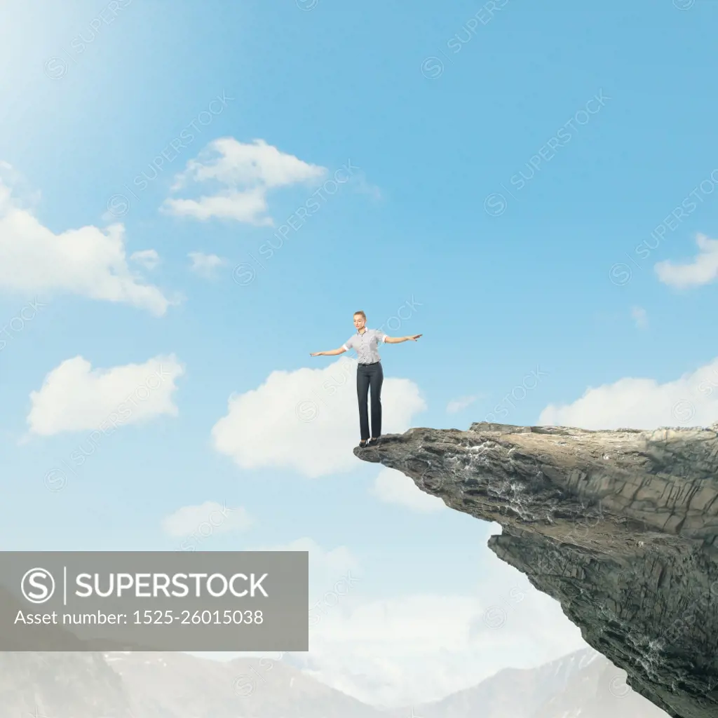 Risky business. Young businesswoman balancing on edge of hill top