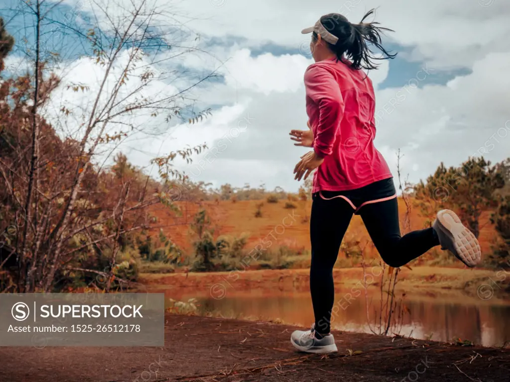 Athletic woman running on forest trail by the lake. Female runner running in nature in the morning. Workout Healthy lifestyle concept.