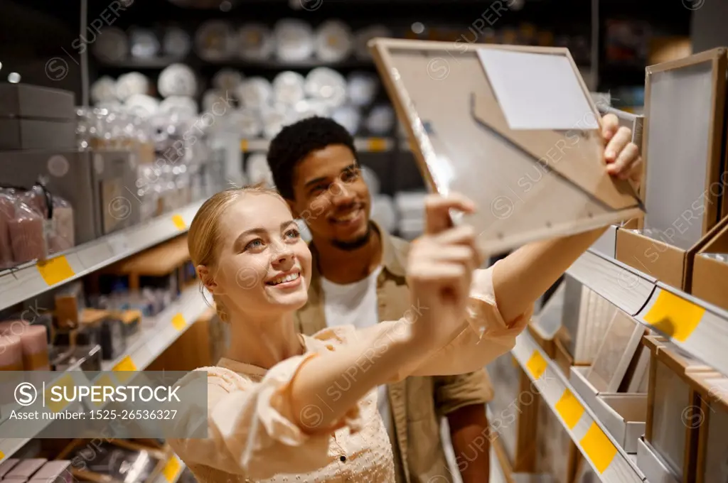 Young couple buying picture photo frame at shop. Multi ethnic woman man choosing decor for housing. Young couple buying photo frame at shop