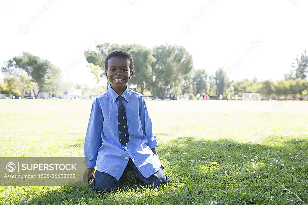 Portrait of boy kneeling on grass in sunlit park