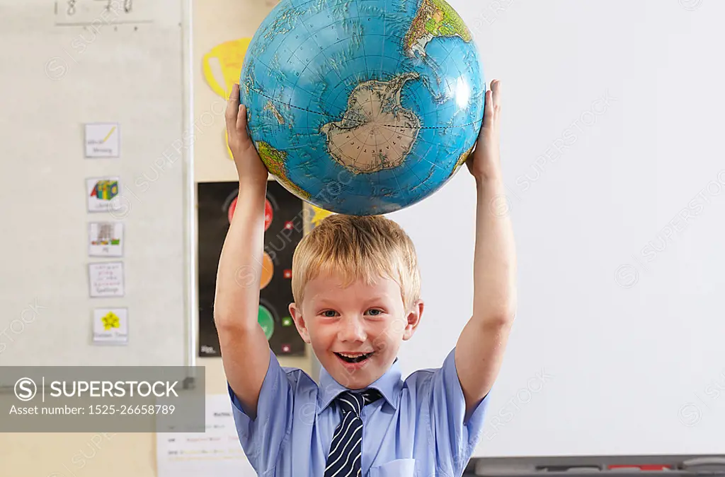 School boy holding globe over his head in a classroom