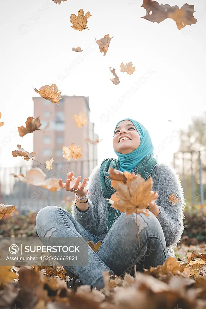 Young woman sitting in park throwing autumn leaves